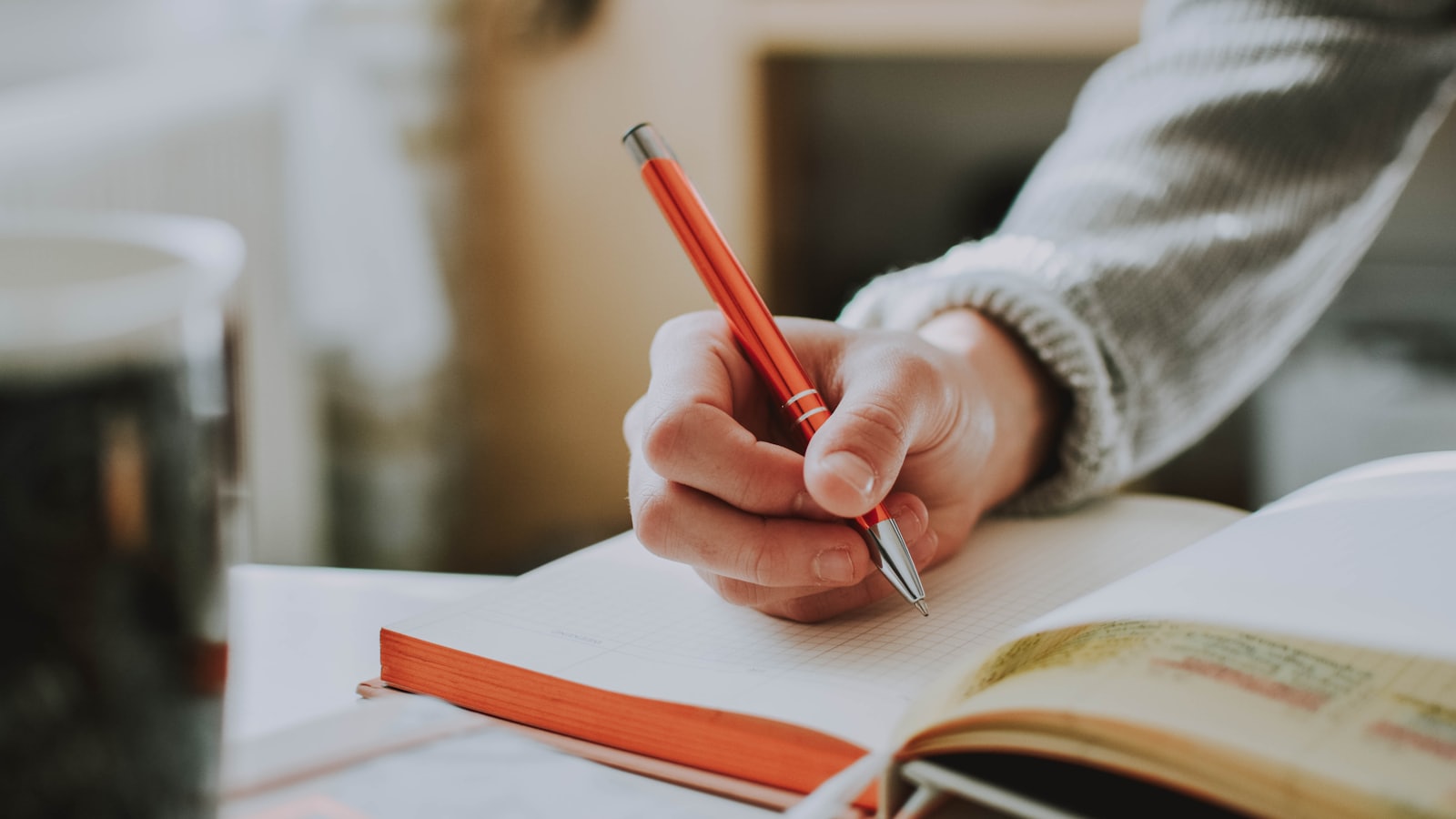 A hand writing in a squared notebook with a red ballpoint pen