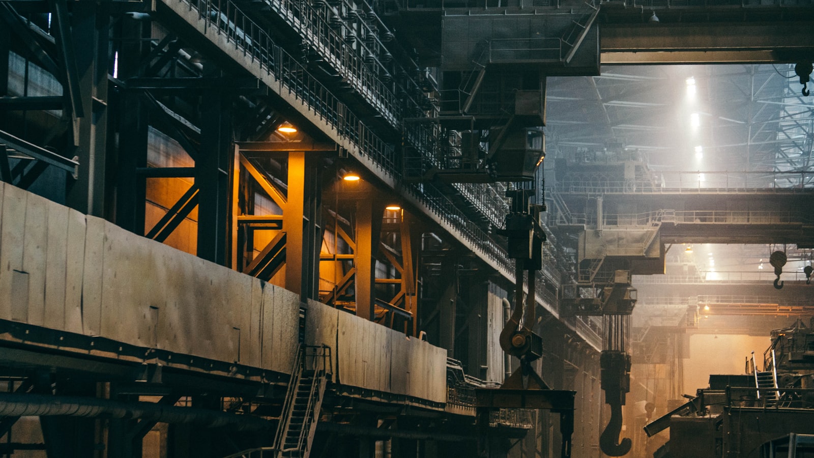 The interior of a heavy industrial plant, with overhead crane hooks and gantries lit from above