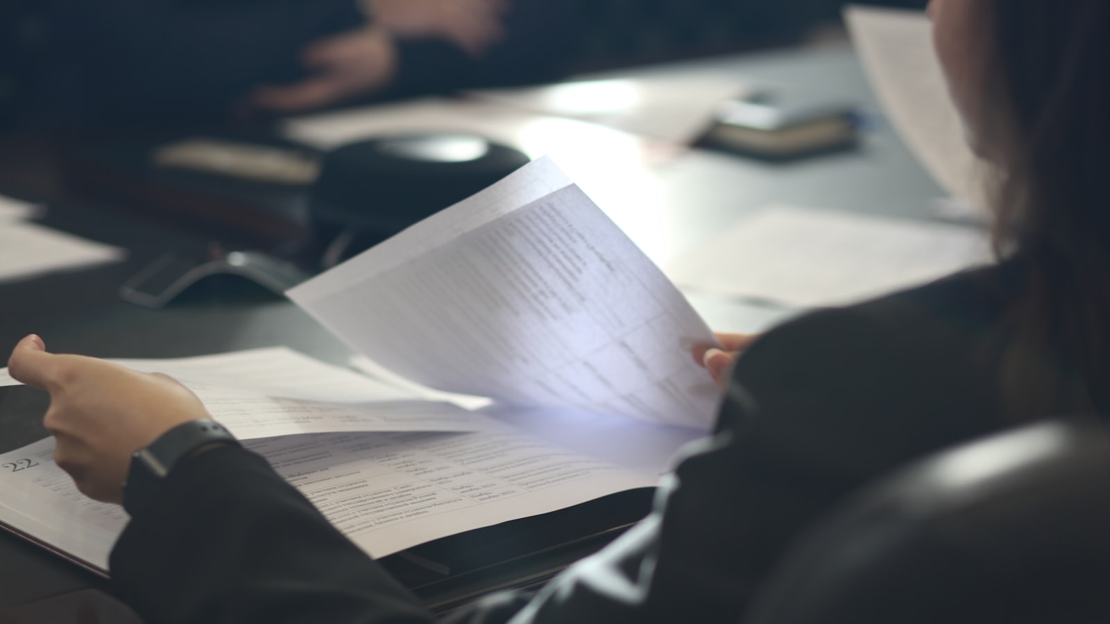 A person turning the pages of a printed report at a meeting table