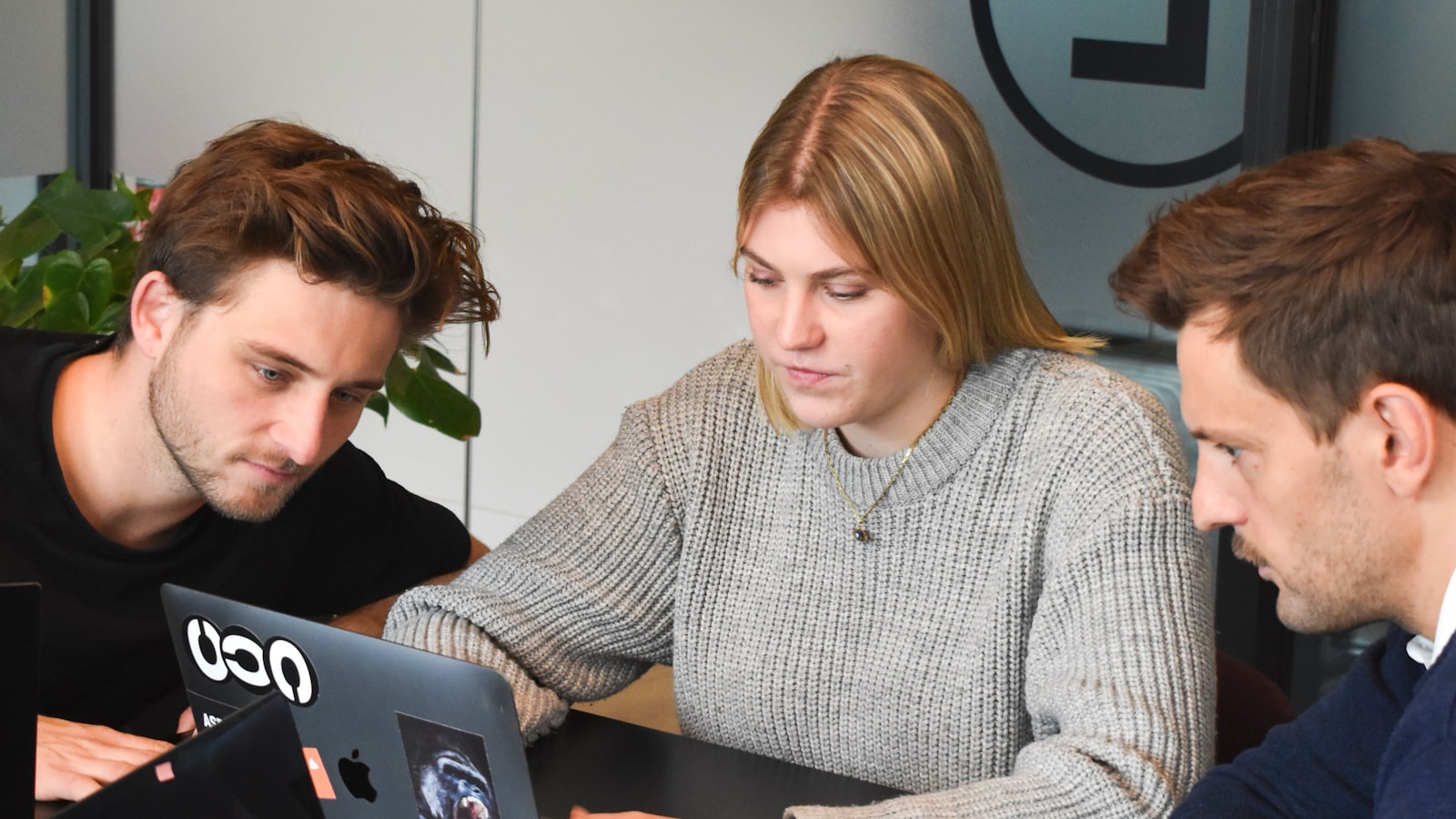 Three colleagues sharing one laptop screen at an office table