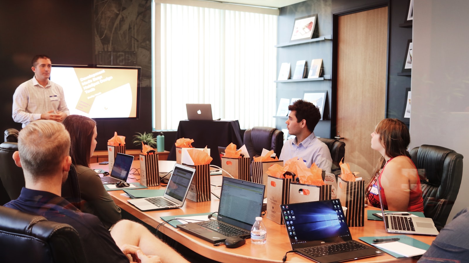 A trainer standing at the head of a boardroom table while participants work on laptops