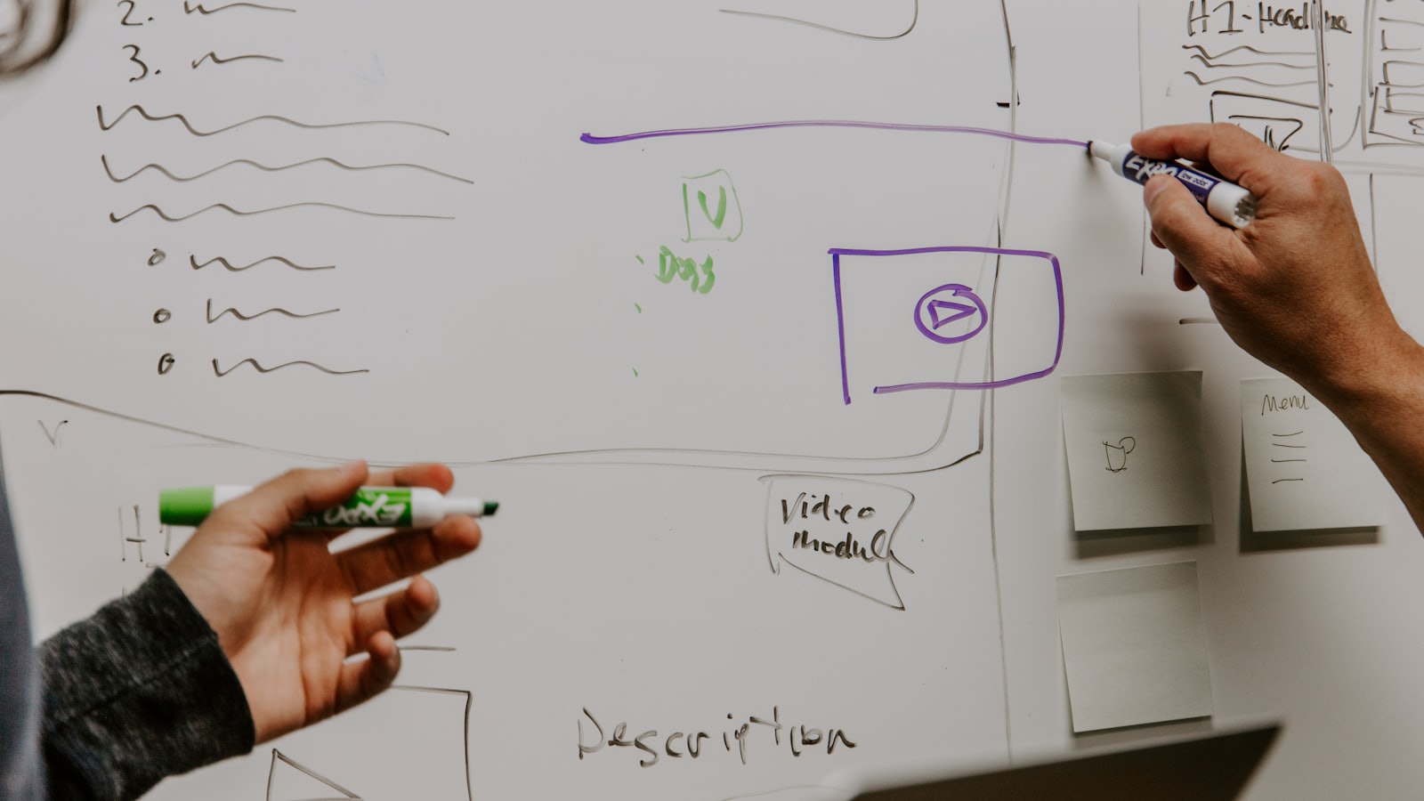 Two people sketching a page layout and a video module on a whiteboard in marker pen